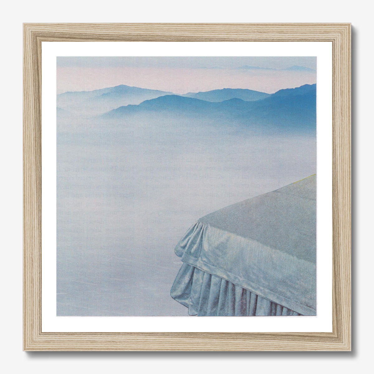Framed wall art featuring a misty mountain landscape with layered blue peaks and a pale pink sky, matted with a white border and set in a light natural wood frame.