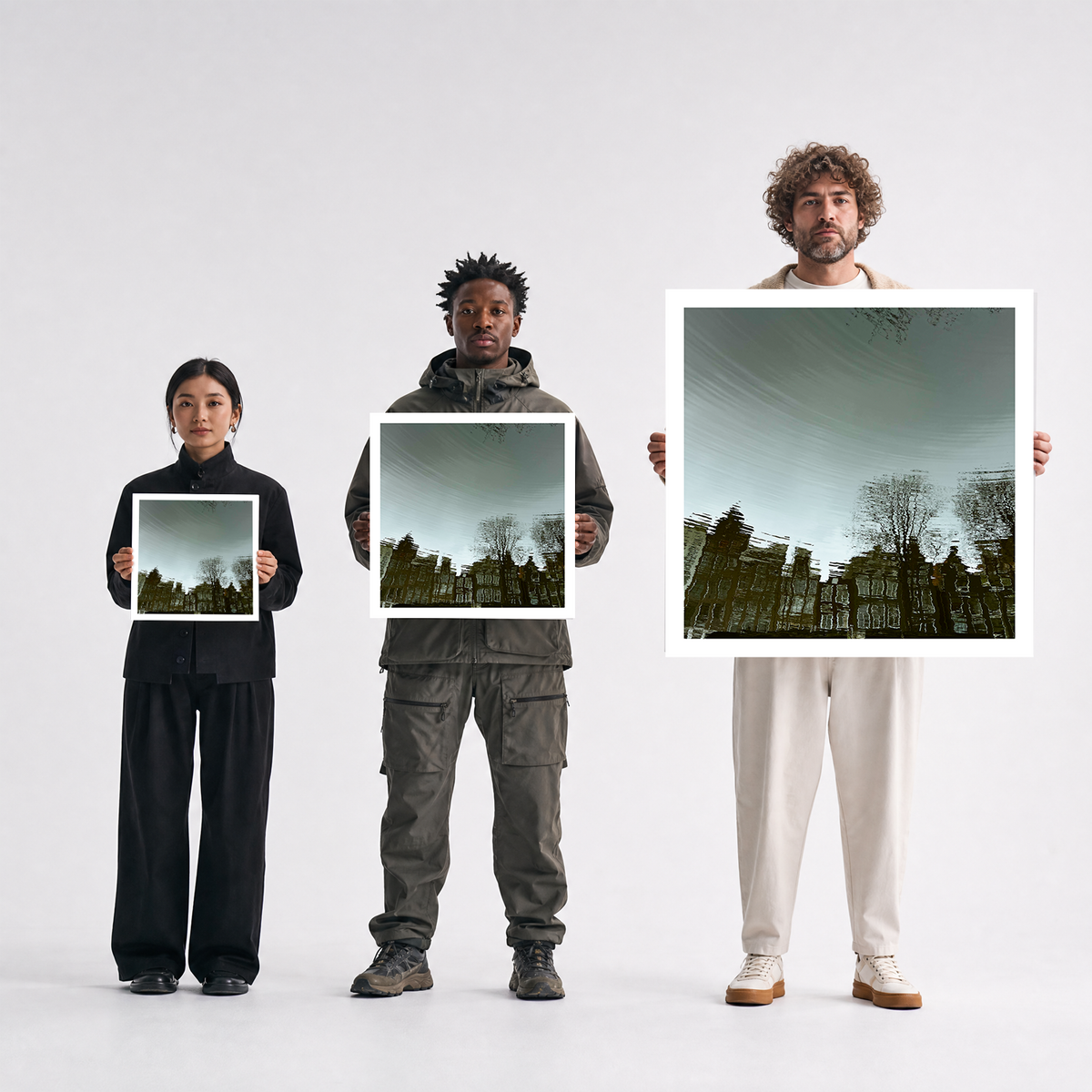 Scale comparison photo showing the 12x12, 20x20, and 40x40 print sizes of 'Canal' by Sunday Morning, held by three models for size reference.